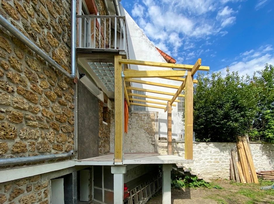 Terrasse en bois en cours de construction, adossée à un bâtiment en pierre de taille