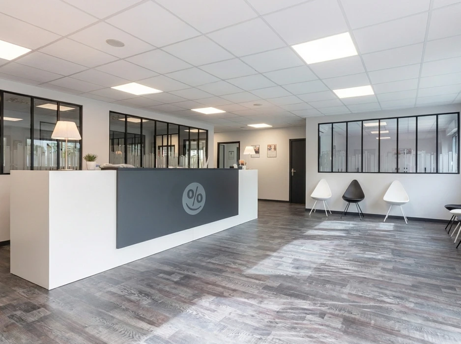 Accueil professionnel moderne avec comptoir de réception blanc et gris anthracite orné d'un logo smiley en forme de pourcentage