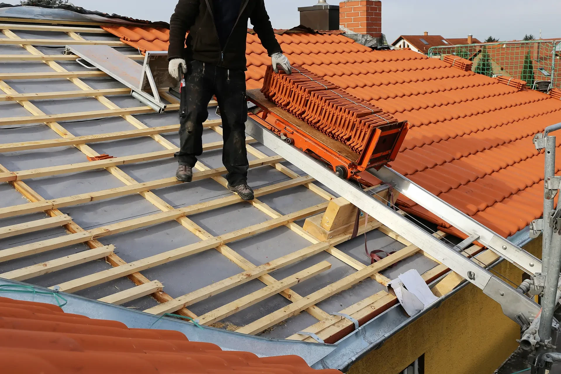 Un ouvrier en construction installe des tuiles sur le toit en ardoise sur la Nouvelle maison sous un ciel ensoleillé