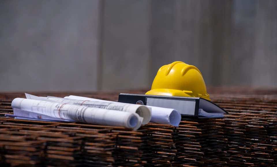 Deux professionnels du b&acirc;timent examinent des plans architecturaux dans un bureau ensoleill&eacute;